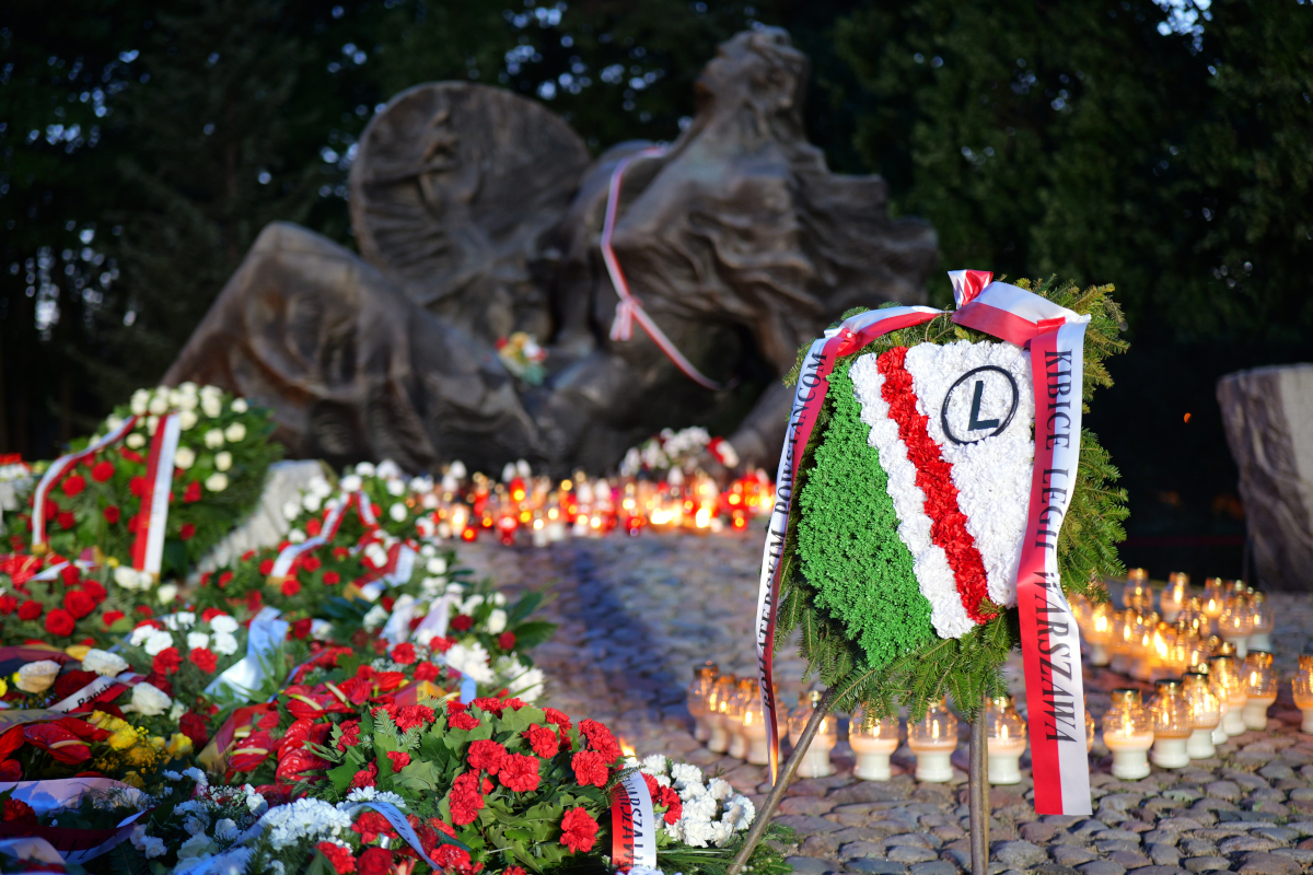 Płonący znicze i wieńce przy Pomniku Polegli Niepokonani na Woli